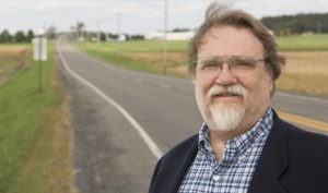 man with glasses and beard standing next to a road