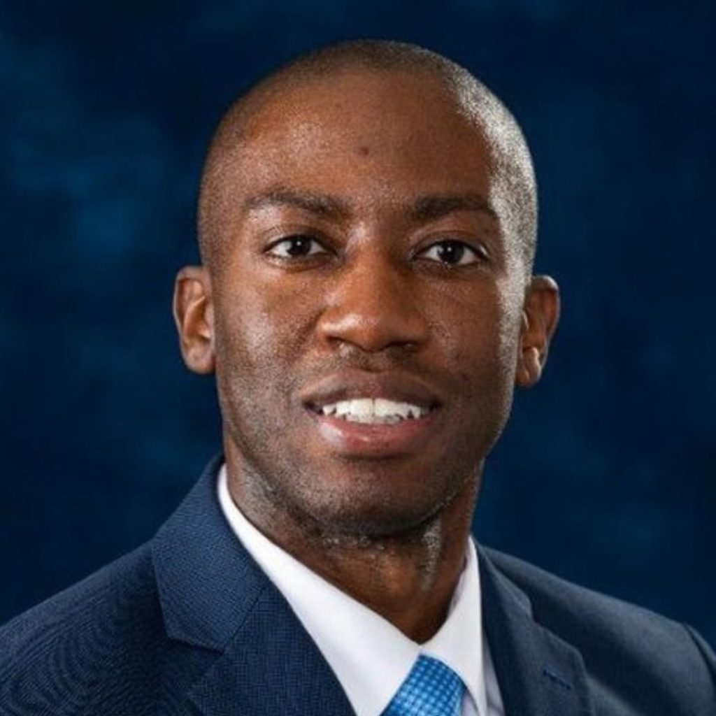 Portrait of a smiling man in a navy suit.