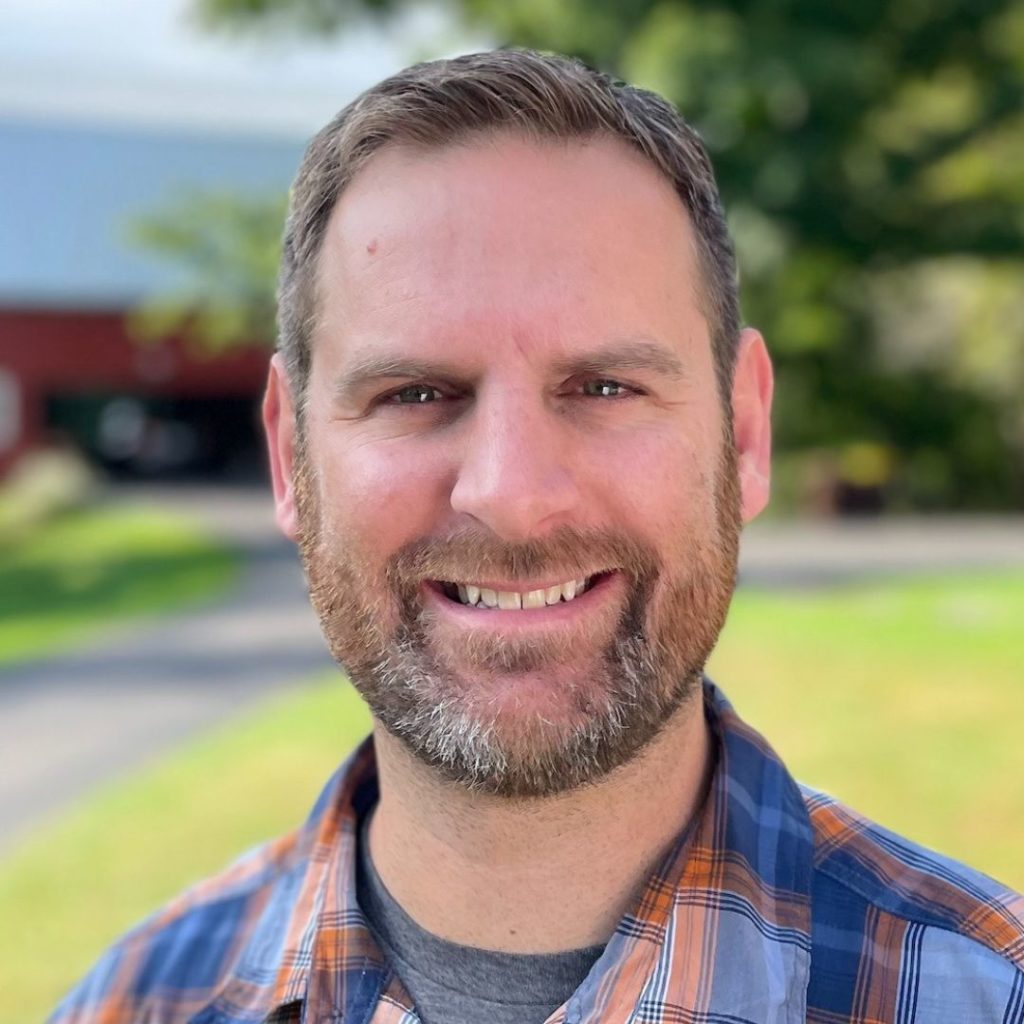 Portrait of a smiling man with a short beard in a blue and orange plaid button-down.