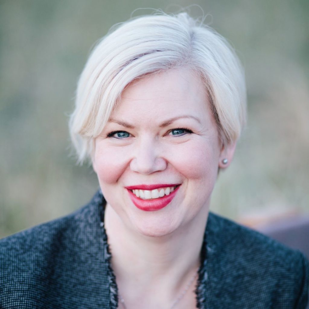 Portrait of a smiling woman with short white hair wearing a navy jacket.