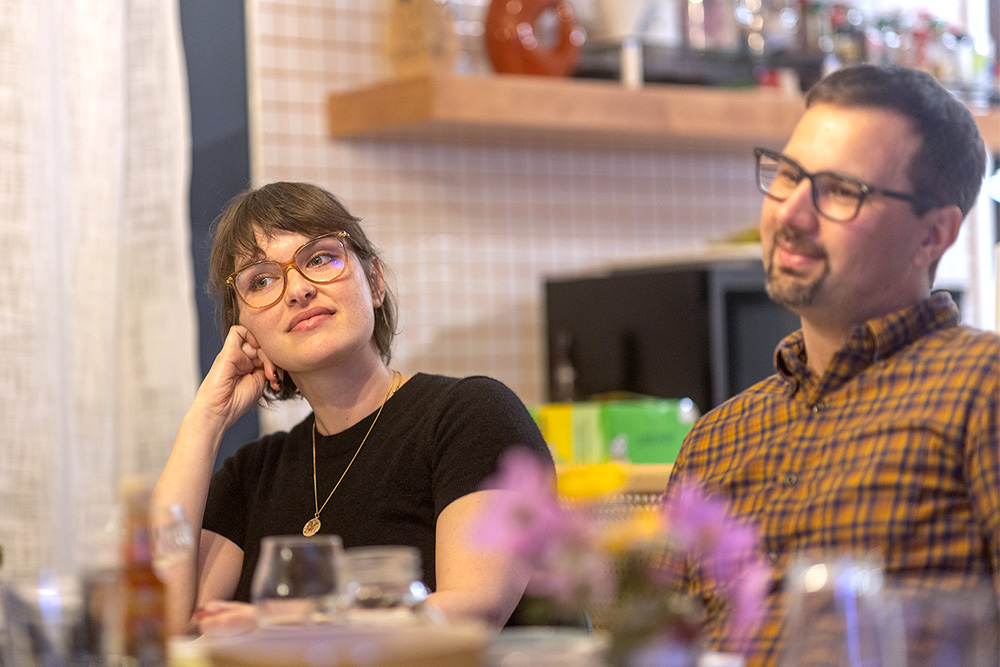 Megan Dean wearing a black shirt and glasses sits next to a friend at a table.