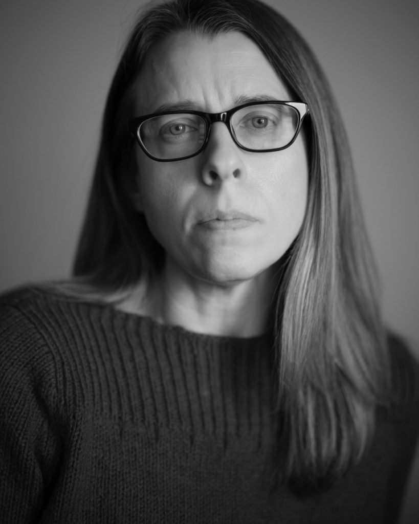 Black and white close up of a woman with long hair and glasses.