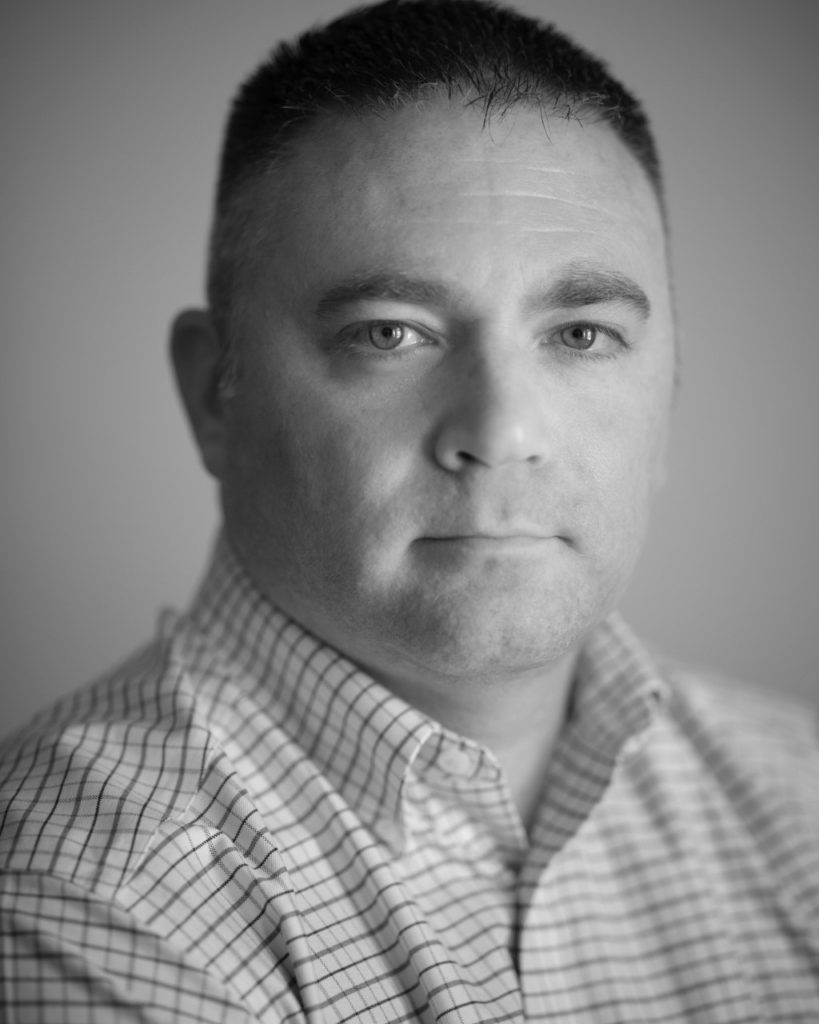 Black and white close up of a clean-shaven man with short hair.