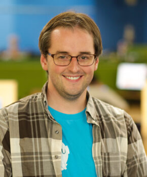man with brown hair and glasses wearing blue shirt with flannel shirt over it